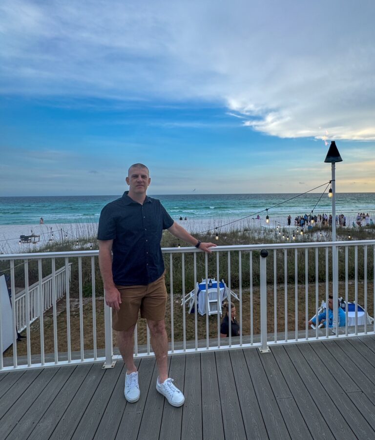 a man standing on a deck with a railing and a beach and people